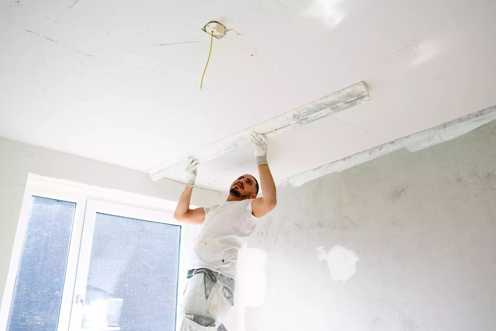 Stukadoor egaliseert een plafond met een lange rei